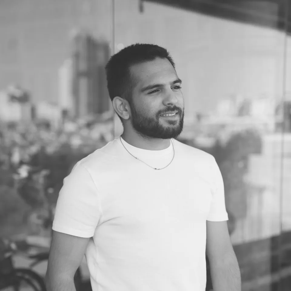 Black-and-white portrait of Liel Amar in a white T-shirt, smiling, in front of a glass wall